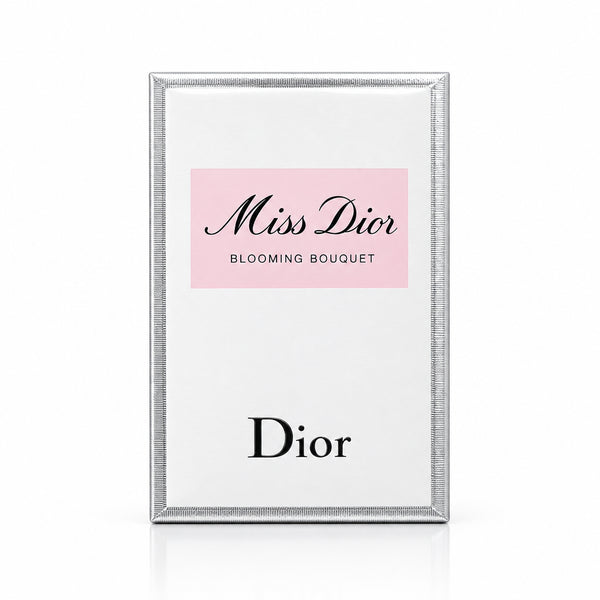 Dior Miss Dior Blooming Bouquet perfume box standing upright on a marble surface, with pink roses in a vase on the left and a blurred Dior container in the background.