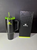 Black Stanley mug with green lid and straw next to a matching black box on a gray background