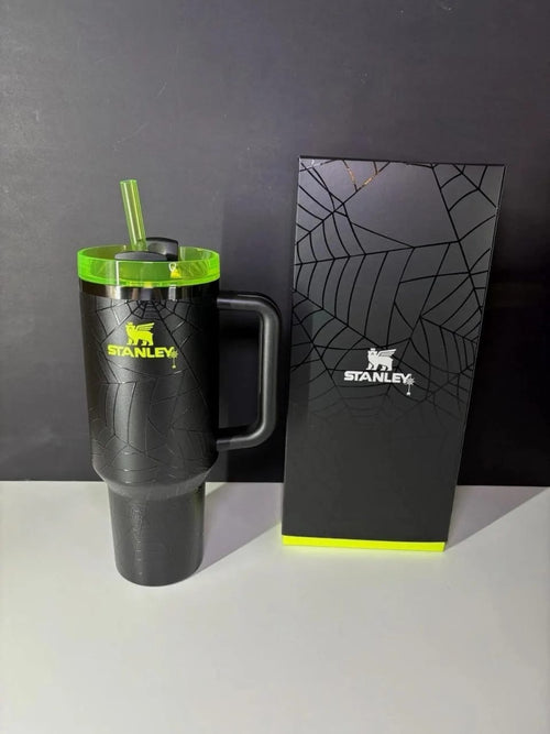 Black Stanley mug with green lid and straw next to a matching black box on a gray background