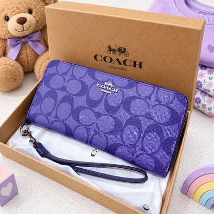 A purple Coach wallet with the signature C logo pattern, resting inside its brown cardboard box on white tissue paper.