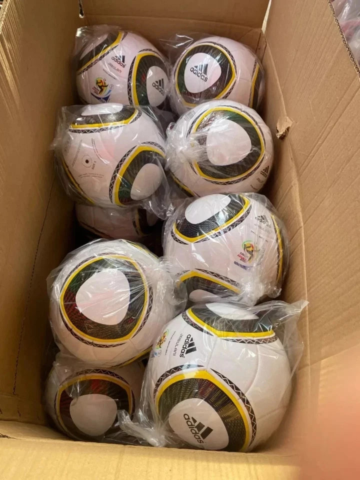 A cardboard box filled with multiple Adidas soccer balls wrapped in clear plastic, photographed from above.