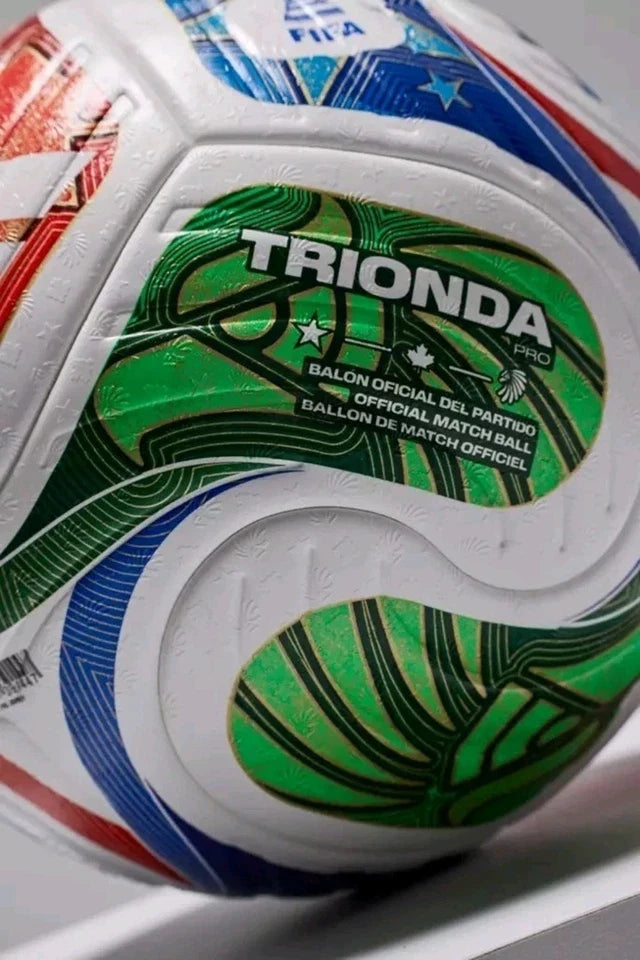 Close-up of a FIFA official match ball with the word TRIONDA prominently printed on a green panel, showing white, blue, and red patterned sections.
